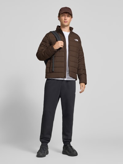 Männermodel trägt Regular Fit Jacke in Stepp-Optik Modell 'ACONCAGUA' von The North Face, Dunkelbraun, Stehkragen, Logo-Stitching, Ganzkörperansicht von vorne.