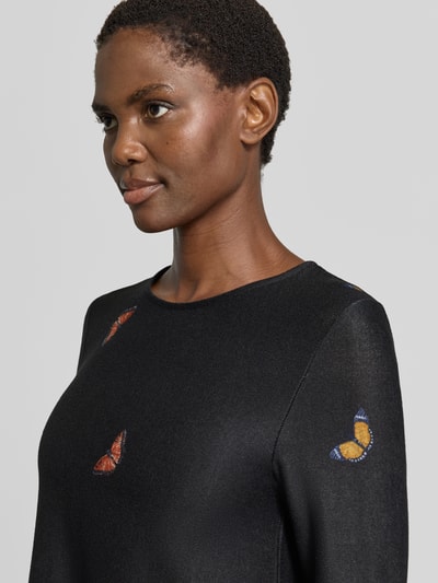Frauenmodel trägt Minikleid mit Rundhalsausschnitt von Apricot, Schwarz mit bunten Schmetterlingsmotiven, Material-Mix mit Stretch-Anteil, Nahaufnahme Oberkörper.