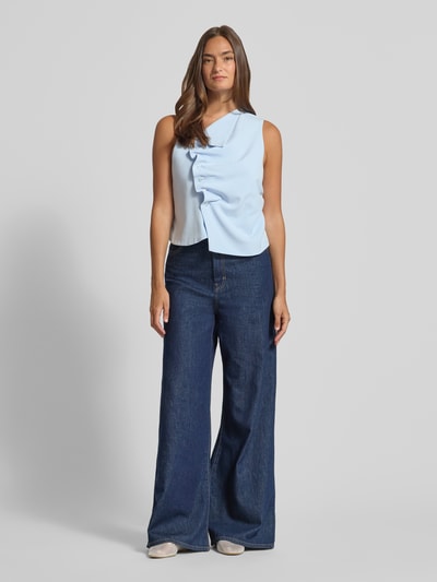 Frauenmodel trägt Top in asymmetrischem Look von My Essential Wardrobe im hellen Blau, Material-Mix mit Viskose-Anteil, Knopfleiste, Körpernahe Passform, glatte Textur, Rückenlänge bei Größe 36: 51 cm, Schulterbreite: 31 cm, Brustweite: 42 cm, Ganzkörperansicht von vorne.