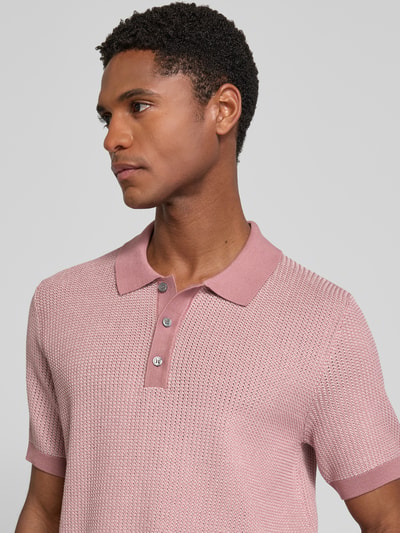 Męski model nosi koszulkę polo Slim Fit Poloshirt mit Strukturmuster model 'Brianoro' von JOOP! COLLECTION z bawełny, z fakturowanym wzorem i listwą guzikową, detal z logo, różowy kolor, krój slim fit, długość tyłu w rozmiarze M: 70 cm, zbliżenie na górną część ciała.