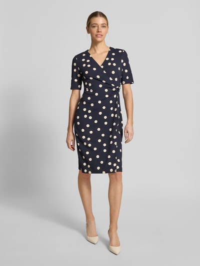 Vrouwenmodel draagt Tailliertes Midikleid in Wickeloptik van s.Oliver BLACK LABEL, allover polka dot patroon, v-hals, o-ring applicatie, kort mouw, donkerblauw met witte stippen, taillierter fit, midi lengte, vooraanzicht volledige lichaamsopname.