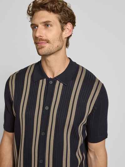 Männermodel trägt Regular Fit Poloshirt aus reiner Baumwolle Marc O'Polo × DFB Travel Collection mit Streifenmuster, Nahaufnahme Oberkörper.