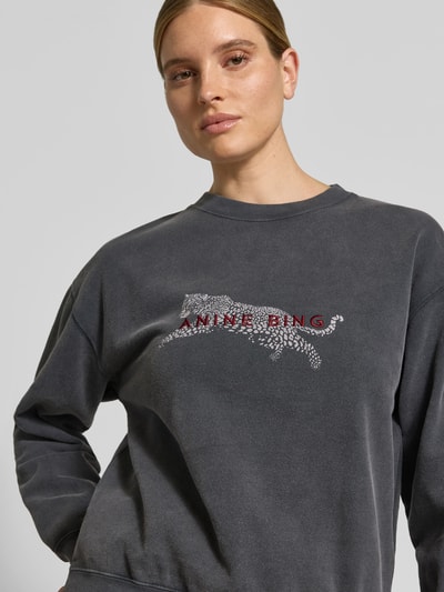 Vrouwenmodel draagt Oversized Sweatshirt aus reiner Baumwoll van Anine Bing in antraciet met print en labeldetail, elastische boorden, close-up bovenlichaam.