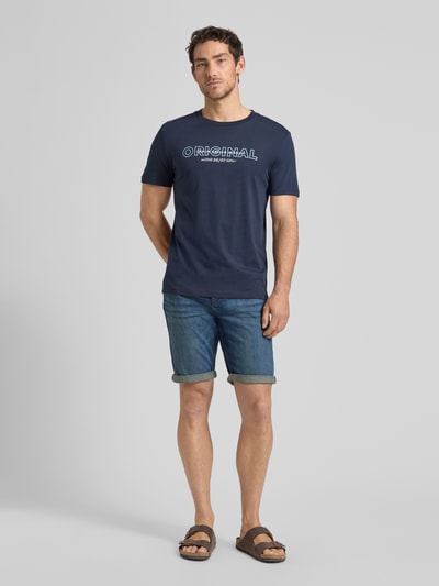 Männermodel trägt Regular Fit Jeans Bermudas aus Baumwoll-Mix von Tom Tailor, Denim-Optik, 5-Pocket-Design, Label-Patch, Ganzkörperansicht von vorne.