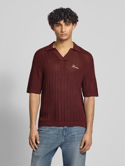 Męski model nosi Slim Fit Poloshirt in Crochet-Optik od REVIEW, bawełna, krój slim fit, półrękaw, logo, kolor bordowy, widok od przodu, zdjęcie całej sylwetki.