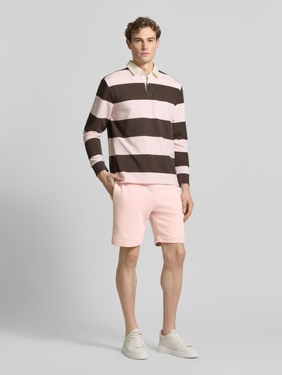 Männermodel trägt Regular Fit Sweatshorts aus Baumwoll-Mix van Lacoste in effen lichtroze sweatstof met label patch, elastische tailleband met trekkoord, zijzakken en achterzak, geheellichaamsaanzicht van voren.