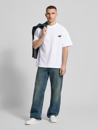 Männermodel trägt Regular Fit T-Shirt mit Logo-Stitching von ANOTHER COTTON LAB in Weiß, kombiniert mit Jeans, Nahaufnahme Oberkörper. Reine Baumwolle, Rundhalsausschnitt, Rückenlänge 70 cm bei Größe M.