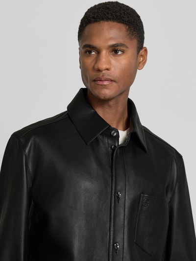 Męski model nosi Regular Fit Lederjacke aus echtem Lammleder Modell 'C-MOVITZ' od BOSS, czarne gładkie lico, wykładany kołnierz, wytłoczone logo, brustasza, listwa guzikowa, krój regular fit, materiał skóra jagnięca, Nahaufnahme górnej części ciała.