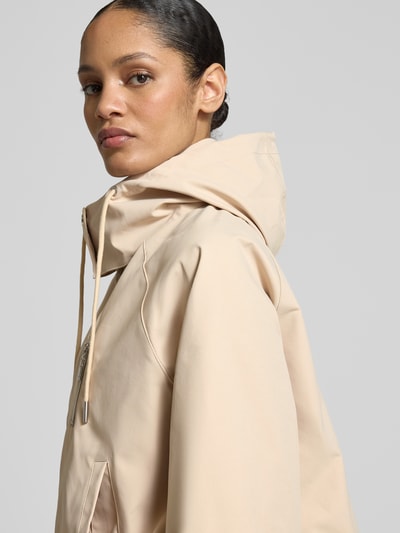 Vrouwenmodel draagt Jacke mit Kapuze und Zweiwege-Reißverschluss van monari in beige met steekzakken, relaxed fit, detailopname schouder. Ruglengte maat 36: 56 cm, schouderbreedte: 45 cm, borstwijdte: 54 cm, mouwlengte: 58 cm.