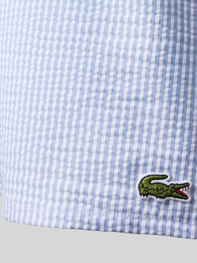Männermodel trägt Badeshorts aus Baumwoll-Mix von Lacoste, Mehrfarbig, Gestreift, Logo-Applikation, Seersucker, Nahaufnahme Bein.