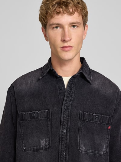 Männermodel trägt Regular Fit Jeanshemd aus reiner Baumwolle von Replay in Schwarz mit Kentkragen und Brusttaschen, Nahaufnahme Oberkörper.