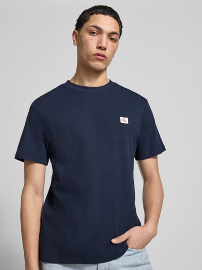 Männermodel trägt Regular Fit T-Shirt mit Logo-Patch von Calvin Klein Jeans aus Baumwoll-Mix, Strukturmuster, Rundhalsausschnitt, Ganzkörperansicht von vorne.
