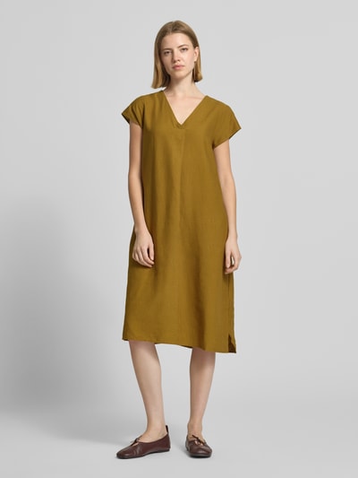 Frauenmodel trägt knielanges Leinenkleid mit V-Ausschnitt Modell 'Ina' von Soyaconcept im Leinen-Mix mit Viskose-Anteil, Loose-Fit, Seitliche Schlitze, Farbe Senf, glatte Oberfläche, Ganzkörperansicht von vorne.