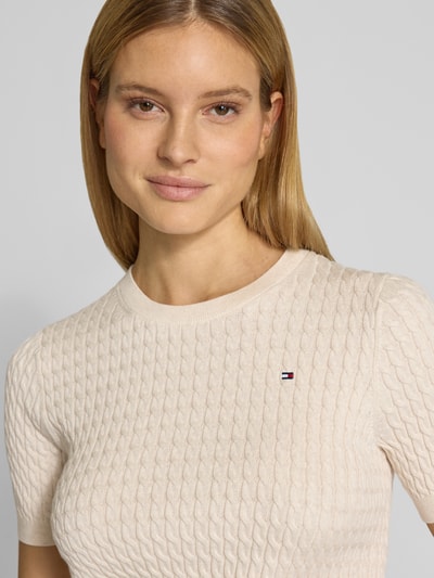 Frauenmodel trägt Slim Fit T-Shirt aus reiner Baumwolle von Tommy Hilfiger in Unifarbe mit Zopfmuster, Logo-Detail, Nahaufnahme Oberkörper.