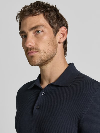Mężczyzna nosi Slim Fit Poloshirt aus Baumwoll-Mix in Strick-Optik von Matinique, mieszanka bawełny, krój slim fit, imitacja dzianiny, wykończenia: elastyczne, z krótkim rękawem, Długość tyłu w rozmiarze M: 72 cm, ciemnogranatowy, faktura prążkowana, Nahaufnahme górnej części ciała.