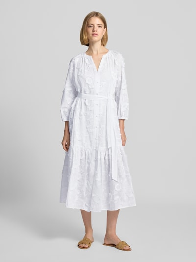 Vrouwenmodel draagt relaxed fit midi-jurk met florale siergarnering van comma, materiaalmix met katoen, tuniekhals, 3/4-mouw, knoopsluiting, ruglengte maat 36: 119 cm, borstwijdte maat 36: 60 cm, mouwlengte maat 36: 47 cm. Ganzkörperansicht von vorne.
