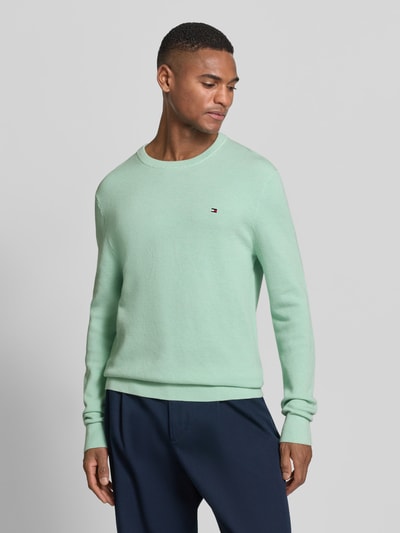 Männermodel trägt Regular Fit Strickpullover aus reiner Baumwolle von Tommy Hilfiger in Optik: Unifarben, Strickoptik, Logo-Detail, Ganzkörperansicht von vorne.
