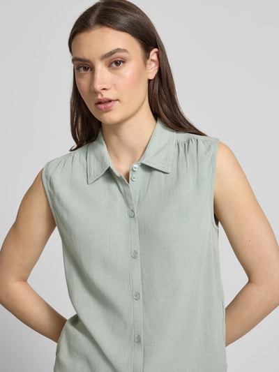 Frauenmodel trägt Regular Fit Leinenbluse ohne Ärmel Modell 'SIESTA' von Only in Melange-Optik aus Viskose-Leinen-Mix mit Hemdblusenkragen, einreihiger Knopfleiste und Raffungen, Nahaufnahme Oberkörper.