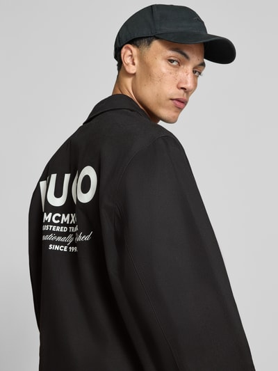 Männermodel trägt schwarze Regular Fit Bomberjacke / Blouson aus reiner Baumwolle Modell 'Biyo2631' von HUGO Blue, Ganzkörperansicht Rückansicht.