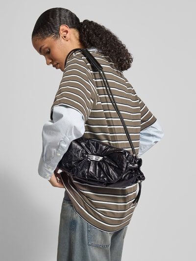 Frauenmodel trägt Shoulder Bag mit Logo-Detail von Diesel in Schwarz mit Raffungen und Magnetverschluss, Nahaufnahme Oberkörper, Hauptfach mit Überschlag, Reißverschlussfach innen, Maße ca. 33x17x8 cm.