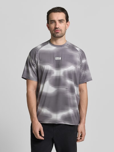 Männermodel trägt Regular Fit T-Shirt mit Logo-Applikation von EA7 Emporio Armani in Grau mit abstraktem Muster, elastischer Material-Mix, Rundhalsausschnitt, Nahaufnahme Oberkörper.