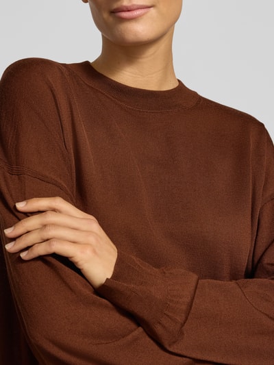 Vrouwenmodel draagt gebreide pullover van zuivere scheerwol in bruin, relaxed fit, Model 'MALESE' van DRYKORN, nahaufnahme bovenlichaam. Context: Dames gebreide pullover van DRYKORN, zuivere scheerwol, relaxed fit, Model 'MALESE', ronde hals, ruglengte bij maat S: 49 cm, mouwlengte bij maat S: 52 cm.