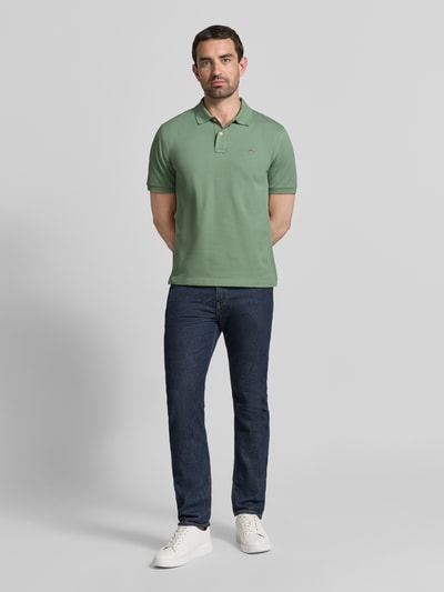 Männermodel trägt Regular Fit poloshirt aus puur katoen van GANT in lichtgroen, effen structuur, donkere jeans, Ganzkörperansicht von vorne.