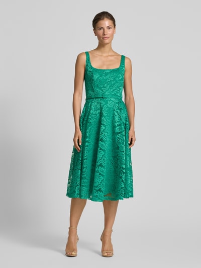 Frauenmodel trägt Knielanges Kleid mit Allover-Spitzen-Besatz von Rinascimento in leuchtendem Grün, taillierter Schnitt, ausgestelltes ärmelloses Design mit abnehmbarem Gürtel, elastischer Material-Mix, Ganzkörperansicht von vorne.