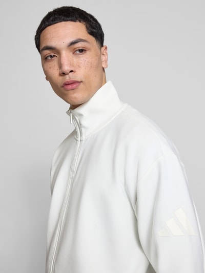 Männermodel trägt Regular Fit Sweatjacke aus reiner Baumwolle von adidas Sportswear in Unifarben mit Logo-Print, Nahaufnahme Oberkörper.