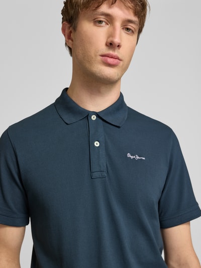 Männermodel trägt Regular Fit Poloshirt aus reiner Baumwolle Modell 'OSCAR' von Pepe Jeans, jednokolorowy, wyhaftowane logo, kołnierzyk polo, dekolt w serek, krótka listwa guzikowa, krótki rękaw, zakończenia rękawów prążkowane, dół z rozcięciami, wykończenie: pika, materiał: czysta bawełna. Nahaufnahme Oberkörper.