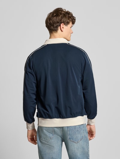 Männermodel trägt Slim Fit Sweatjacke mit Logo-Stitching Modell 'Niagara' von Jack & Jones in donkerblauw met contrastdetails, elastische boorden, staande kraag, steekzakken, ritssluiting, ruglengte 67 cm, mouwlengte 65 cm, ganzkörperansicht rückansicht.
