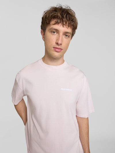 Männermodel trägt Oversized T-Shirt mit Label-Stitching von Pegador aus Baumwoll-Mix in Hellrosa, Rundhalsausschnitt, Nahaufnahme Oberkörper, Rückenlänge bei Größe M 70 cm.