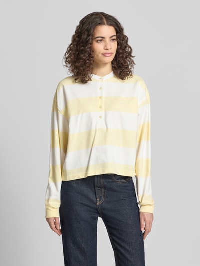 Frauenmodel trägt Relaxed Fit Sweatshirt mit Logo-Stitching Modell 'Varsity' von Calvin Klein Jeans, gelb-weiß gestreift, Baumwolle, Langarm, Knopfleiste, elastische Ärmelabschlüsse, Ganzkörperansicht von vorne.