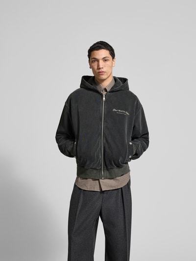 Männermodel trägt Oversized Jeansjacke aus Baumwoll-Mix von Don't Waste Culture, dunkle Farbe, Eingrifftaschen, Ganzkörperansicht von vorne. Rückenlänge bei Größe M 65 cm, Schulterbreite 58 cm, Ärmellänge 67 cm, durchgehender Reißverschluss, elastische Abschlüsse, Druckknopfverschluss an den Taschen.
