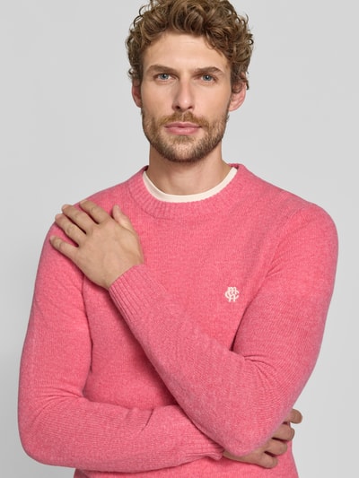 Männermodel trägt Slim Fit Strickpullover aus reiner Wolle mit Label-Stitching von MCNEAL, rosa Farbton, gerippte Abschlüsse, Nahaufnahme Oberkörper.
