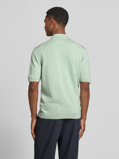 Männermodel trägt Slim Fit Poloshirt aus reiner Bio-Baumwolle von Armedangels in Mintgrün, unifarben, Feinstrick, Ganzkörperansicht Rückansicht.