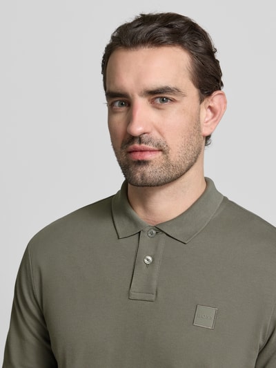 Männermodel trägt Slim Fit Poloshirt aus Baumwoll-Mix Modell 'PASSERBY' von BOSS Orange in Olivgrün, Label Stitching, Nahaufnahme Oberkörper.
