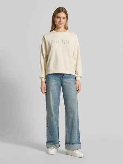 Modelka nosi Regular Fit Sweatshirt mit Ziersteinbesatz Modell 'Banu' od Soyaconcept, kremowy odcień, gładka faktura, napis FRESH, elastyczne wykończenia, krój regular fit z modalem, widok całej sylwetki z przodu.