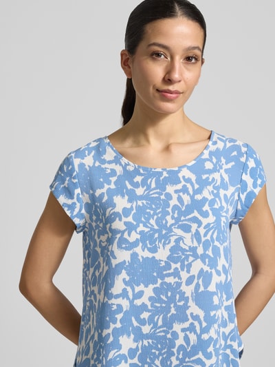 Modelka nosi Relaxed Fit Blusenshirt in Crêpe-Verarbeitung Modell 'VIC' od Only, efekt: wzór na całej powierzchni, dekolt w łódkę, krótkie rękawy, zaokrąglone wykończenie, wykończenie materiału: krepa, niebiesko-biały wzór, przód, zbliżenie górnej części ciała.