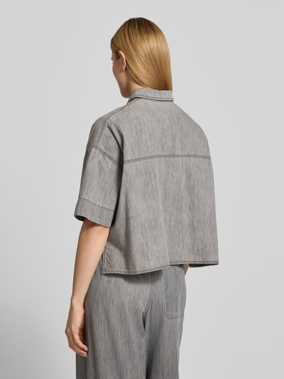 Kobiece modelka nosi bluzkę jeansową z bawełny, pudełkowy krój, model 'YARIKA' od Drykorn, kołnierzyk koszulowy, listwa guzikowa, długość tyłu 53 cm, długość rękawów 22 cm, widok całej sylwetki z tyłu.
