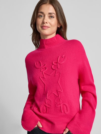 Frauenmodel trägt Strickpullover mit Stehkragen von Christian Berg Woman in Pink, lockere Passform, Strukturmuster, Nahaufnahme Oberkörper.