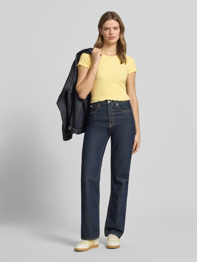 Kobiece modelka nosi damski t-shirt Slim Fit T-Shirt mit Viskose-Anteil Modell 'EMMA' od Only, jednokolorowy, żółty, faktura w paski, okrągły dekolt, krótki rękaw, zakończenia z falbanką, żakard, mieszanka materiałów z dodatkiem wiskozy, widok całej sylwetki z przodu.