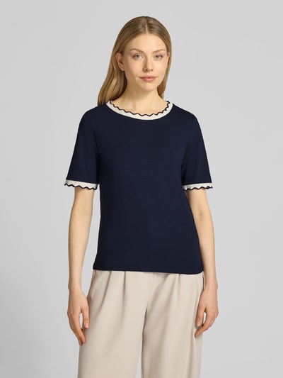 Modelka nosi T-Shirt mit Rundhalsausschnitt und Wellensaum von More & More, bawełna z elastanem, krój regular fit, ciemnogranatowy, widoczne falowane obszycia przy dekolcie i rękawach, długość tyłu w rozmiarze 36: 57 cm, zdjęcie całej sylwetki z przodu.