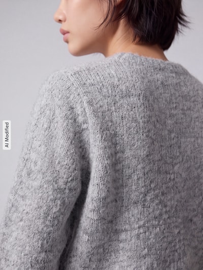 Frauenmodel trägt Regular Fit Strickjacke mit Woll-Anteil Modell 'NOVAH' von VERO MODA, graue melierte Struktur, Nahaufnahme Rückenansicht, KI-modifiziertes Bild.