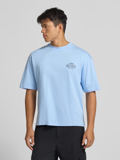 Männermodel trägt Regular Fit T-Shirt aus reiner Baumwolle mit rückseitigem Print von REVIEW in Hellblau, Logo-Detail, Nahaufnahme Oberkörper