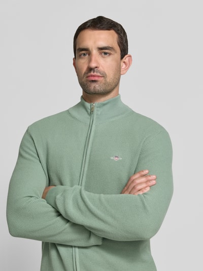 Męski model nosi Regular Fit Strickjacke aus reiner Baumwolle od GANT, zielony odcień, wyrazista faktura, zbliżenie górnej części ciała