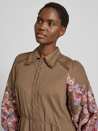 Frauenmodel trägt Hemdblusenkleid mit Bindegürtel Modell 'SOMELLU' von YAS aus brauner Baumwolle, Blumenmuster an Ärmeln, Nahaufnahme Oberkörper. A-Linie, Hemdblusenkragen, Knopfleiste, Bindegürtel, Rückenlänge 89 cm, Brustweite 50 cm, Ärmellänge 68 cm.