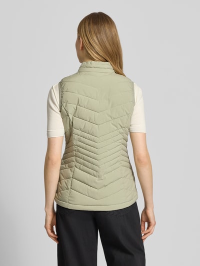 Frauenmodel trägt Steppweste mit 10.000 mm Wassersäule Modell 'GS109' von G.I.G.A. DX in Hellbeige, Stehkragen, Ganzkörperansicht Rückansicht, Slim Fit, dezente Steppnähte, Reißverschlusstaschen, Rückenlänge 61 cm, Schulterbreite 37 cm, Brustweite 49 cm, glatte texturierte Optik.