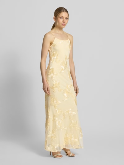 Modelka kobieca nosi Eng anliegendes Abendkleid mit florale Details Modell 'QUINN' od Vero Moda, kolor jednolity, krój dopasowany, długość maxi, dekolt kwadratowy, cienkie ramiączka, prosty dół, jasny żółty z kwiatowymi detalami, całkowity widok z przodu.