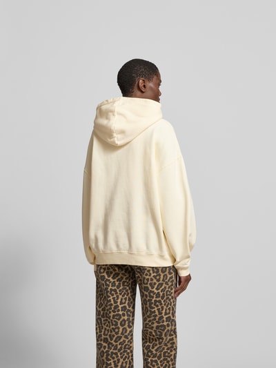 Frauenmodel trägt Oversized Hoodie aus reiner Baumwolle von Anine Bing in Creme mit Label-Detail, elastischen Abschlüssen, Rückenlänge 63 cm, Ganzkörperansicht Rückansicht.